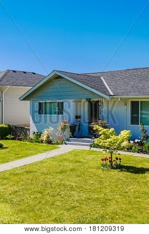 Entrance of modest residential house. Family house with mowed loan on the front yard. Simple residential house in North America with concrete pathway to the entrance