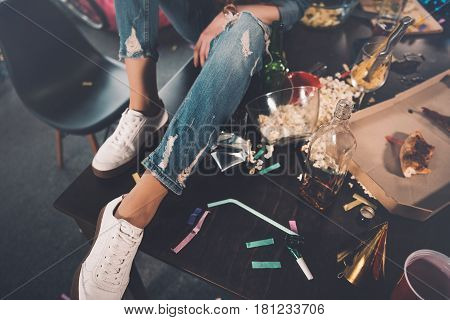 Woman Sitting On Table In Messy Room After Party