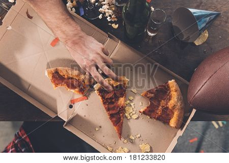 Top View Of Man Eating Stale Pizza In Messy Room After Party