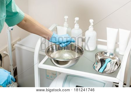 cosmetic Cabinet. beautician preparing for the procedure. the nurse wets the sponge in the water in bowl.  tools in medical basin on table.