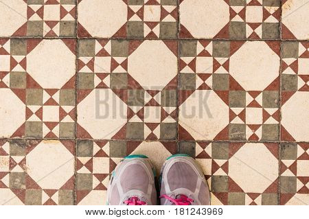Selfie of feet with sneaker shoes on art pattern tiles floor, top view.
