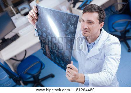 Professional diagnostician. Handsome professional male oncologist looking at the brain x ray images and examining them while putting a diagnosis