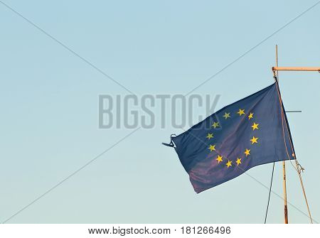 The european union twelve star flag torn and with knots in the wind on blue sky