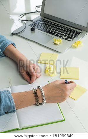 Female hands writing ideas on paper. Woman freelancer working on new project at home office desk with note pad and yellow sticky notes