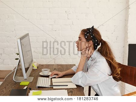 Side view portrait of a female manager with a serious look wearing blue shirt and stylish headscarf working on the computer. Young female entrepreneur working hard to achieve her business goals