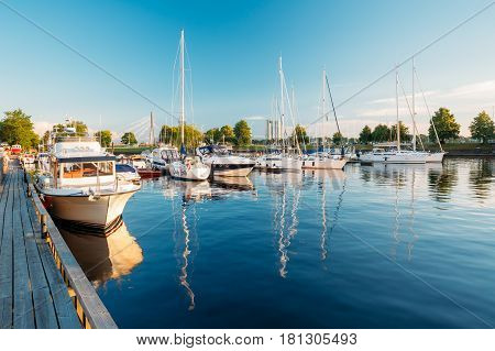 Riga, Latvia - July 1, 2016: Riga, Latvia. Pleasure boats and Yachts Moored At The City Pier Harbour Bay And Quay In Summer Sunny Evening. Reflections From Boats In Water Of Western Dvina River.