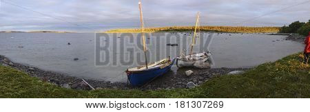 Fishing boats off the coast of the White Sea during the tide. Two old beached wooden rowing boats white and blue weathered and beaten on the shore