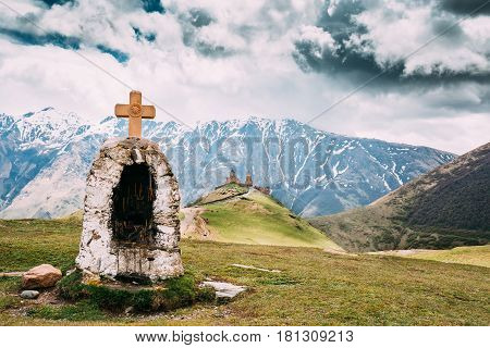 Cross On Stones On Gergeti Trinity Church Or Tsminda Sameba Background. Holy Trinity Church Near Village Of Gergeti In Georgia. Spring Or Summer Season.