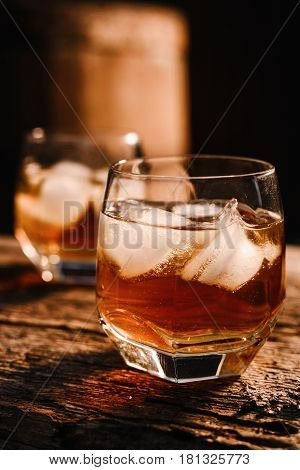 A glass of whiskey with ice on a wooden background close-up in the background of a barrel of whiskey