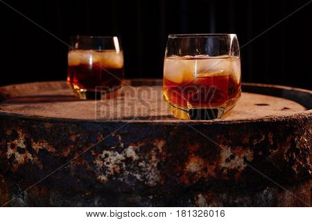 A glass of whiskey with ice on a wooden background close-up in the background of a barrel of whiskey