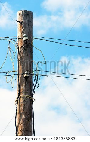 Old wooden pillar with power line against the blue sky. A botched electrical connections