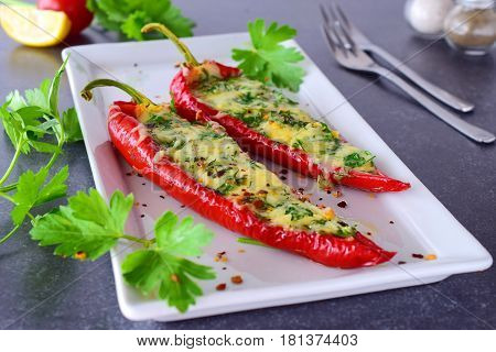 Oven cooked red paprika stuffed with cheese garlic and herbs on a white plate with parcley and cherry tomatoes an abstract grey background. healthy eating concept. Mediterranean. Selective focus.
