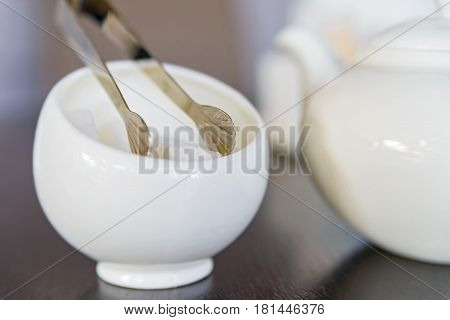 Close up white sugar cubes in white sugar bowl and sugar tongs