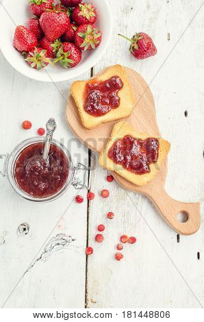 Toasts with strawberry jam for breakfast on white rusric wooden background. Top view.
