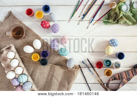 Preparation for Easter. Colorful handmade Easter eggs, paint, brushes on a white wooden background (tabel). Top view. Flat lay style