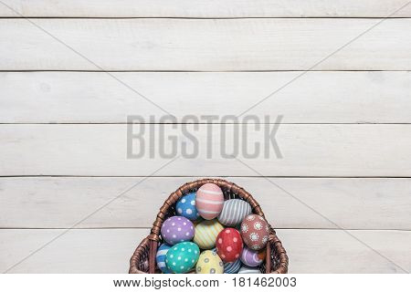 Basket with colorful Easter eggs, painted in handmade on an old white wooden background. Top view, flat lay style