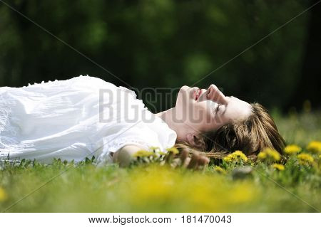 Beautiful young woman is lying on a sunspot spring field. Romantic conception.