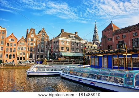 Amsterdam, Netherlands - May 2 2013: Damrak Canal with boats and dancing houses in Amsterdam Netherlands. People on the background