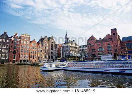 Amsterdam, Netherlands - May 2 2013: Damrak Canal with boats and dancing houses of Amsterdam Netherlands. People on the background