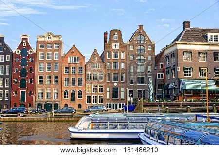 Amsterdam, Netherlands - May 2 2013: Damrak Canal with boats and dancing houses Amsterdam Netherlands. People on the background