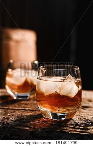 A glass of whiskey with ice on a wooden background close-up in the background of a barrel of whiskey