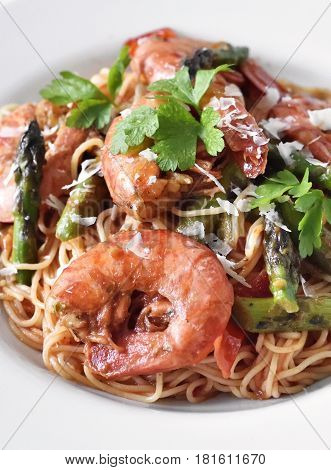 Delicious pasta with great shrimps or prawns and green asparagus on a white plate. Healthy food on a white table or planks. Spaghetti frutti di mare.