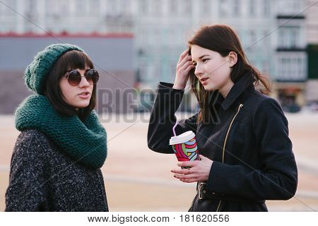 Portrait of two stylish and beautiful girlfriends standing on the street midst of the city