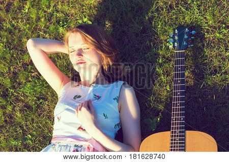 Young Woman Lying On Back In The Sun With Guitar On Green Grass. Toned Photo