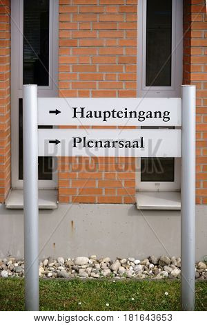 A signpost and direction sign to the main entrance and plenary hall of a department in the university.
