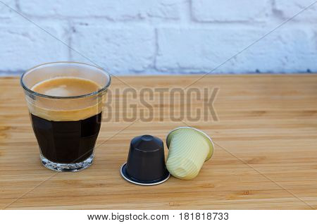 Cup of black coffee with foam and coffee capsules on wooden background.Copy space.
