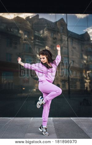 Attractive beautiful young fashion teenager hipster girl fly jump near urban wall background in pink overalls. Fun happy women jump freedom.