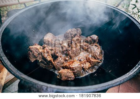 Cooking plov in the cauldron. Only the meat in the cauldron. Field kitchen. Eastern cuisine.