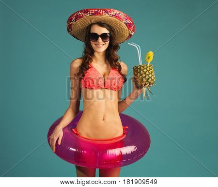 young sexy woman in beach attire with swim ring tropic cocktail looking right isolated on blue background