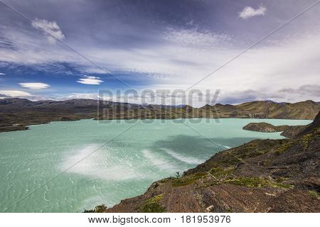panorama of shore of blue lake and sky with windy clouds in patagonia at daylight