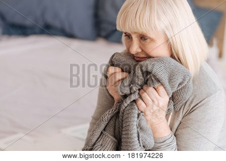 It reminds me of him. Depressed cheerless aged woman holding a knitted jacket and being ready to burst into tears while felling lonely