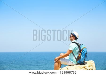 Man looking in to the horizon sitting on rock above the sea. Travel and summer vacation concept