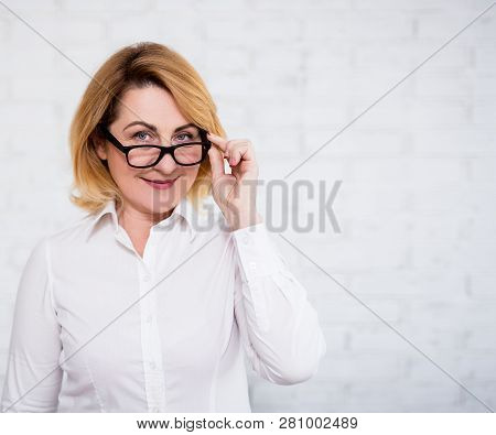 Portrait Of Cheerful Mature Business Woman In Eyeglasses Over White Brick Wall With Copy Space