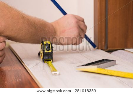 Construcion Worker Measuring Floor Panels Using Ruler And Pencil. Home Renovation Concept.