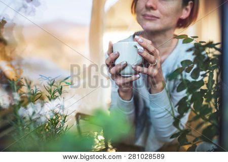 A Young Woman With Cup Of Coffee Looking Out Of A Window. Shot Through Glass.
