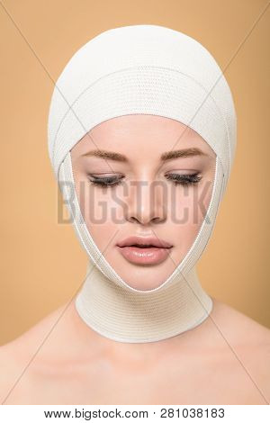 Naked Young Woman With Bandages Over Head Looking Down Isolated On Beige