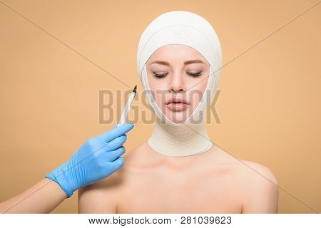 Cropped Shot Of Hand In Latex Glove Holding Scalpel Near Woman With Bandages Over Head Looking Down 