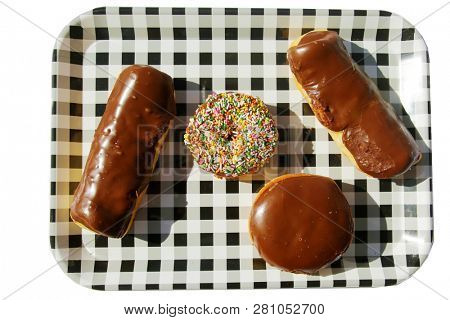 Donut. Donut on a black and white checker tray. Isolated on white. Room for text. Long John Donuts. Cream Filled Donut. Cake Donut with colored sprinkles. Snack Tray.
