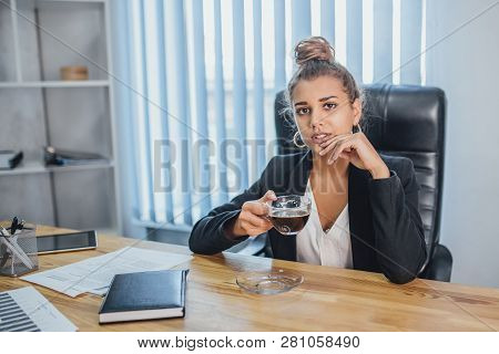 Young Business Girl In The Office Wondering. During This Time She Enjoys A Black, Fragrant Coffee.