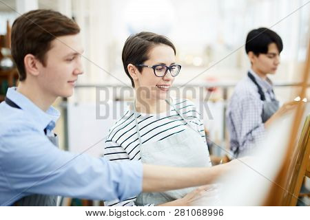 Portrait Of Smiling Female Art Teacher Helping Student Painting Picture On Easel During Class, Copy 