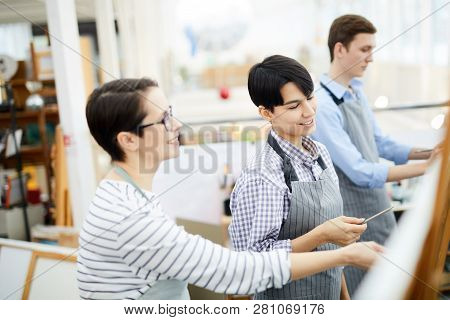 Portrait Of Smiling Young Woman Painting Picture On Easel And Enjoying Art Class In Studio, Copy Spa