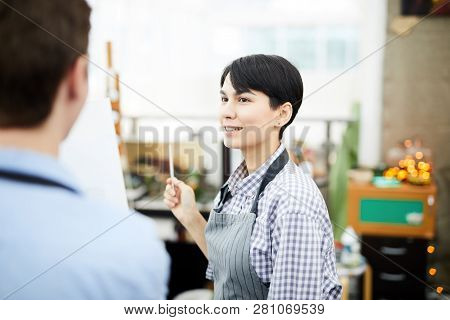 Portrait Of Female Art Teacher Talking To Student Standing By Easel In Class And Smiling, Copy Pace
