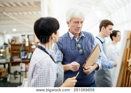 Portrait Of Mature Art Teacher Helping Student Painting Picture On Easel In Art Class, Copy Space