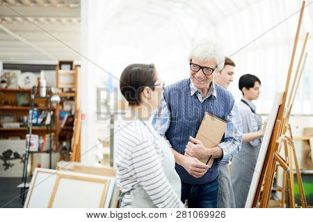 Portrait Of Mature Art Teacher Smiling Happily While Helping Student Painting Picture On Easel In Ar
