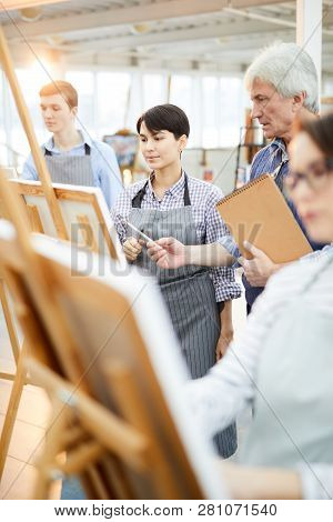 Portrait Of Art Students Painting At Easels In Art Class With Mature Teacher Helping Them, Copy Spac