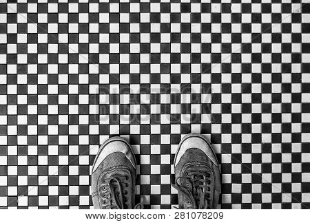 Looking Down From Above Onto A Pair Of Worn Sneakers Or Shoes Standing On A Black And White Mosaic T